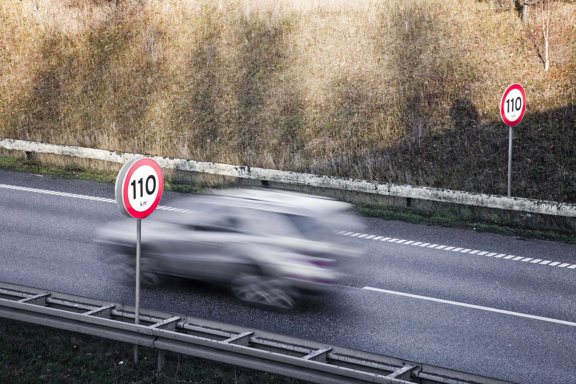 110 kilometer i timen skilt på motorvei med bil i fart midt i bildet