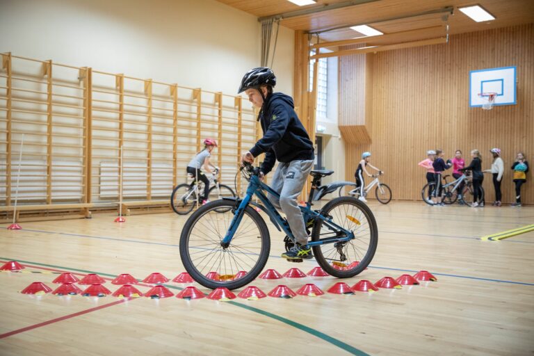 Gutt på sykkel i gymsal. Gutten sykler mellom markører for å mestre sving og balanse.